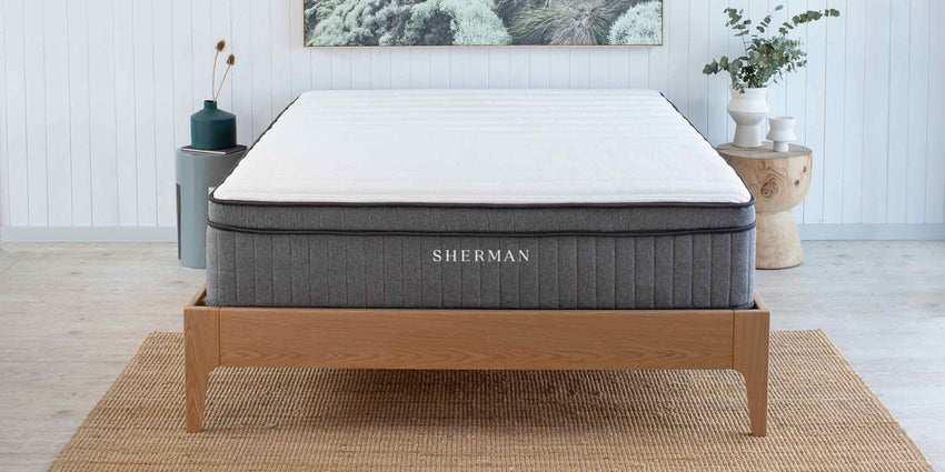 Shows bare Sherman Just Perfect mattress in beach house bedroom scene