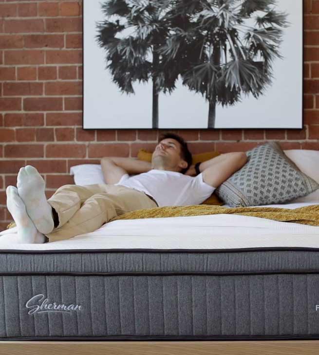 Young man lies down on mattress in Sherman mattress showroom